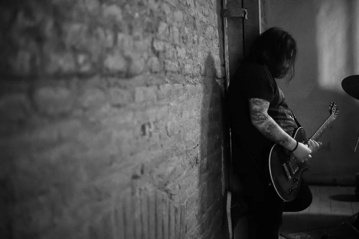 Seba tocando guitarra apoyado en un muro de ladrillo, en blanco y negro